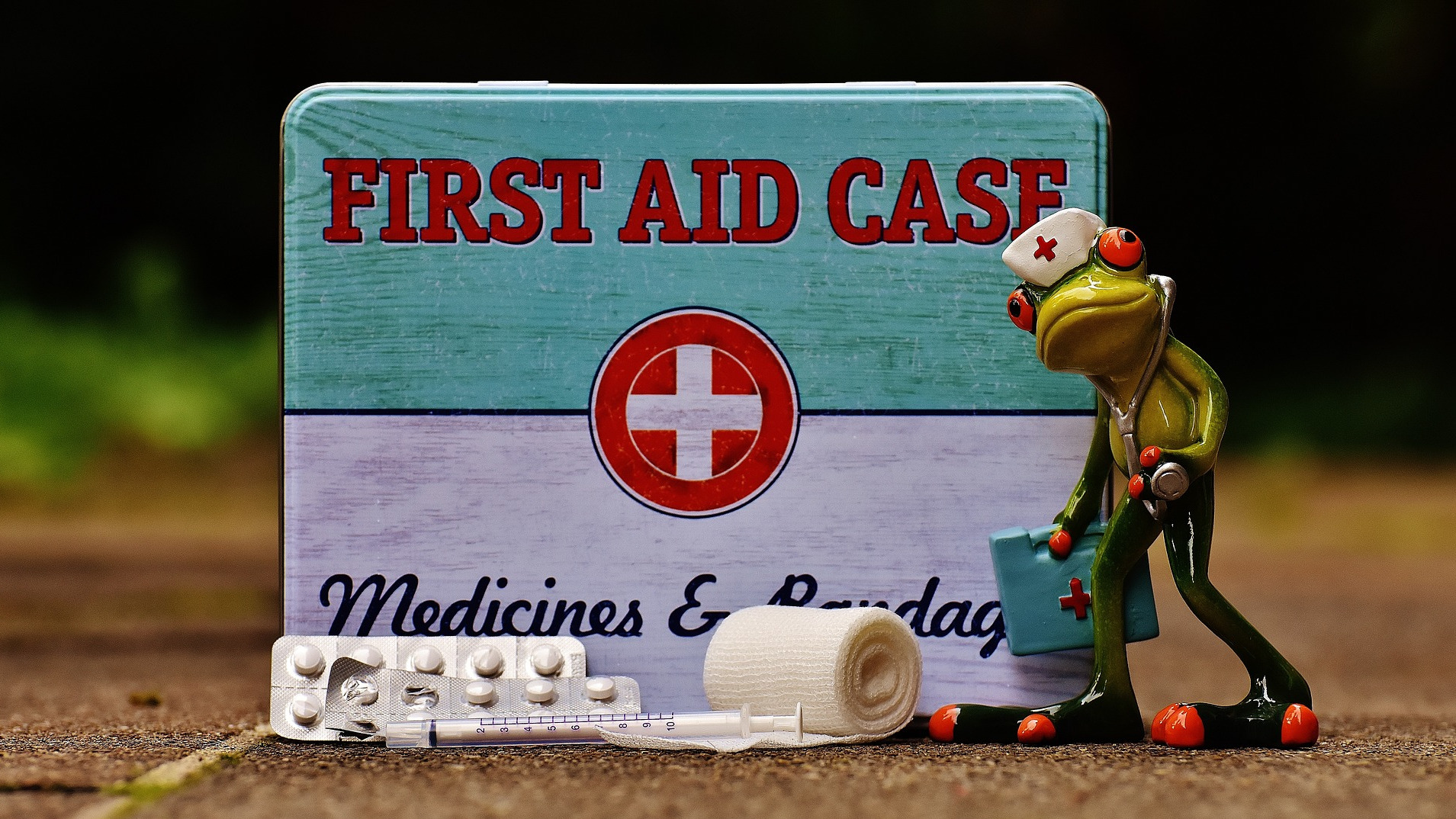 Frog dressed as a doctor standing next to first aid case.