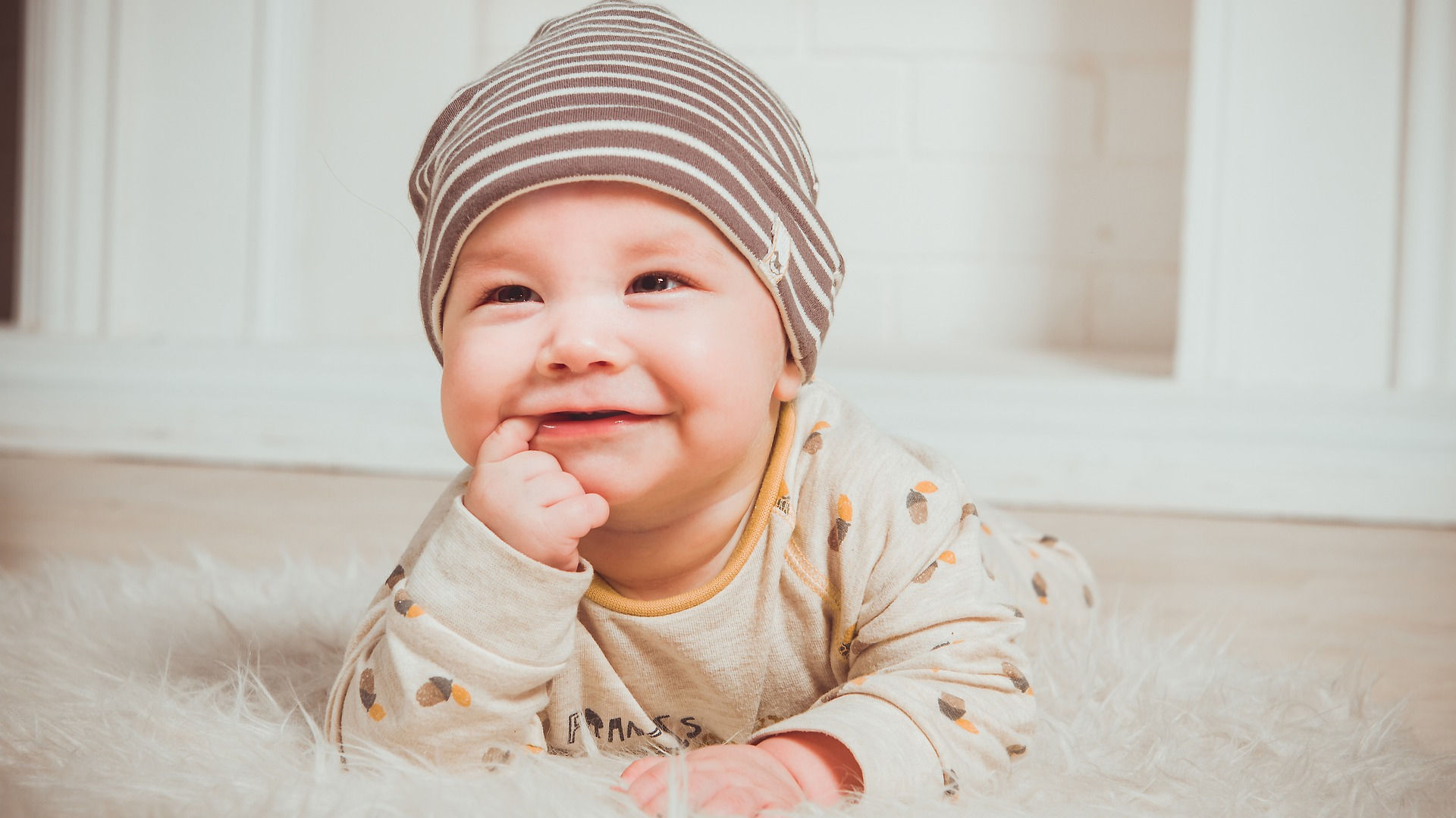 Picture of 6 month old baby laying on ground with finger in mouth